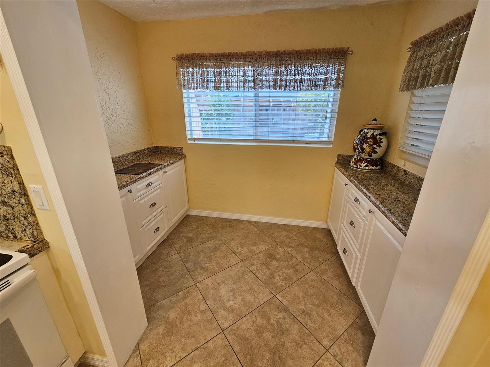 A small kitchen nook features white cabinets, granite countertops, tile flooring, and a window — 6650 Royal Palm Boulevard # 315c, Margate FL 33063, MARGATE, FL