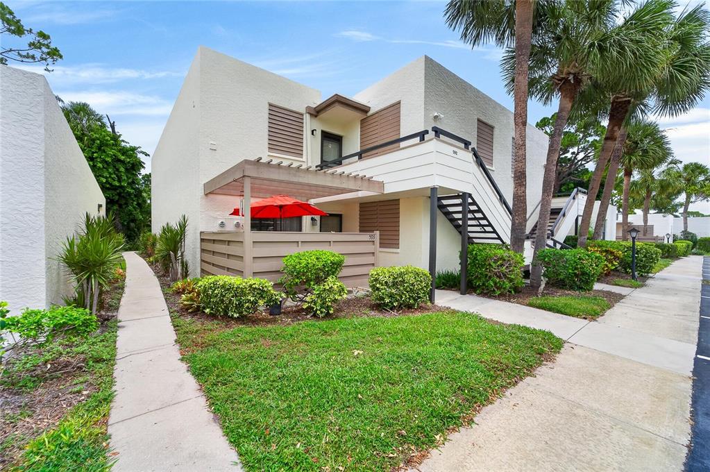 A two-story stucco apartment building features an exterior staircase, a patio with a red umbrella — 593 LAKESIDE DRIVE UNIT 593, BRADENTON, FL