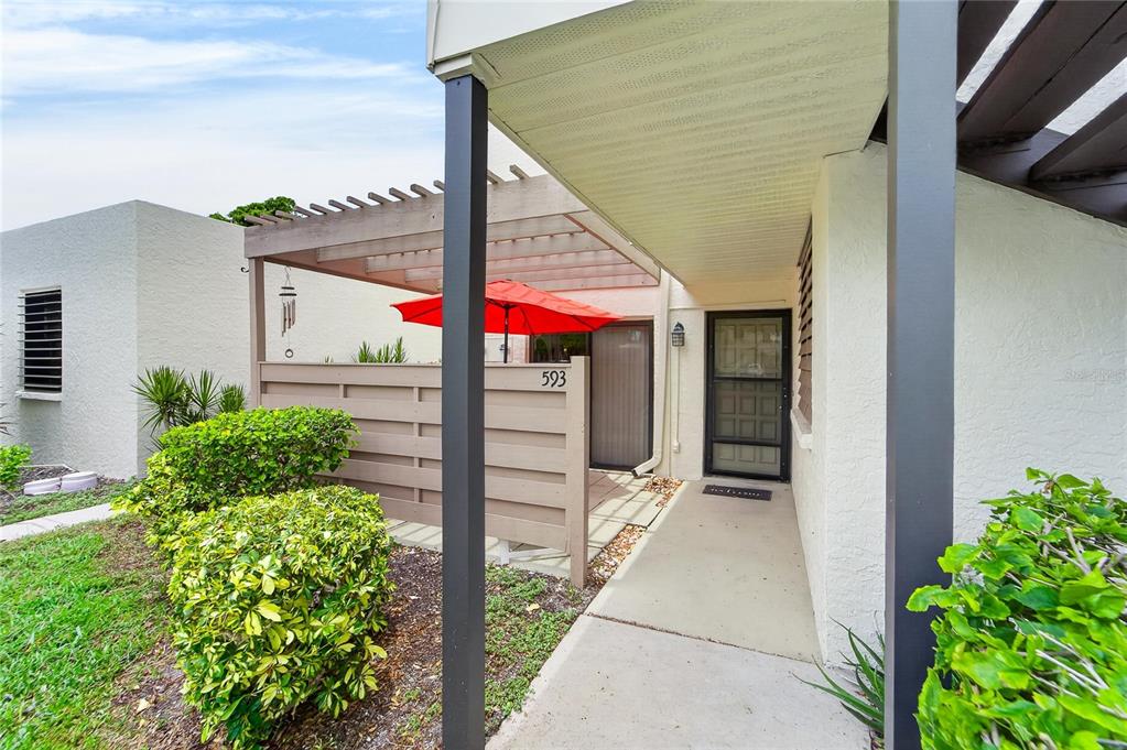 An exterior view of a residential entrance with a patio, pergola, and red umbrella — 593 LAKESIDE DRIVE UNIT 593, BRADENTON, FL