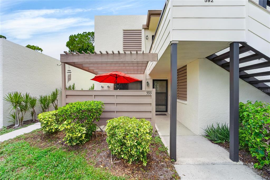 A ground-level apartment entrance features a wooden pergola, a red umbrella, and exterior stairs — 593 LAKESIDE DRIVE UNIT 593, BRADENTON, FL