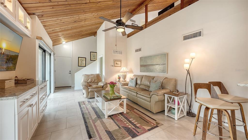 A living room features a vaulted wood-paneled ceiling, tile flooring, a sofa, and bar seating — 218 PASS KEY ROAD UNIT 218, SARASOTA, FL