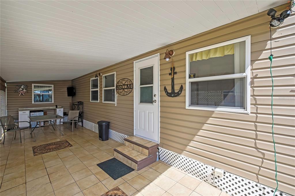 A covered patio features tan siding, tiled flooring, a white door, and nautical wall decor — 800 32ND AVENUE S UNIT 606, ST PETERSBURG, FL