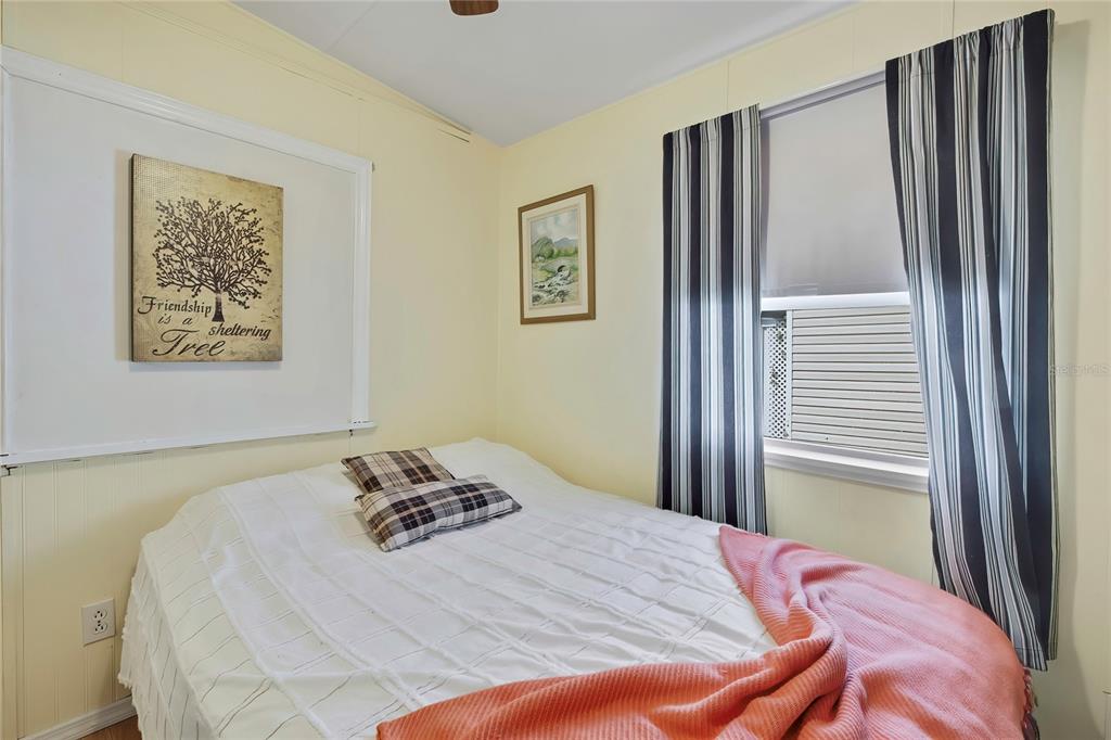 A bedroom features yellow walls, a bed with a white quilt, and striped curtains — 800 32ND AVENUE S UNIT 606, ST PETERSBURG, FL
