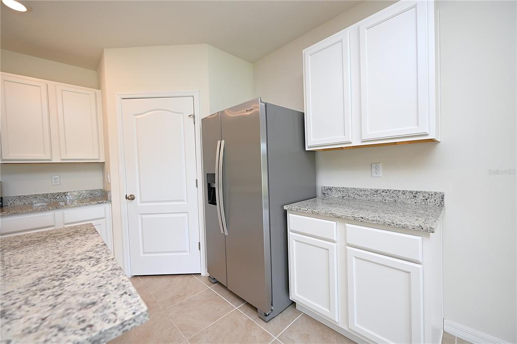 A kitchen features white cabinets, granite countertops, a stainless steel refrigerator, and tile flooring — 3457 MYSTIC POND LOOP, LAKELAND, FL
