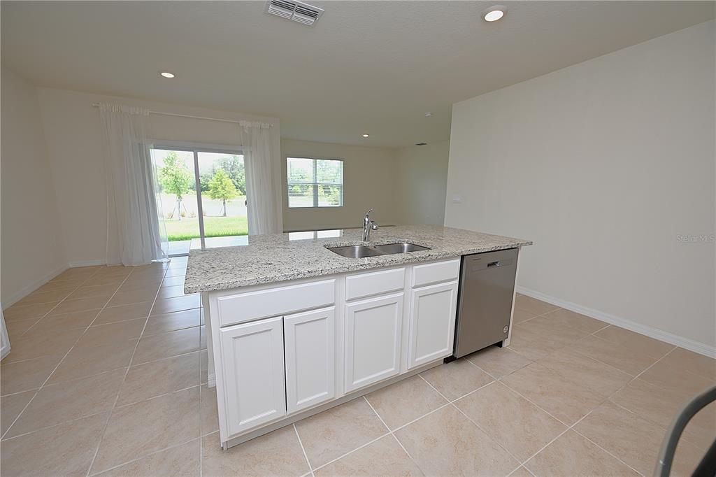 A kitchen island with granite countertops and a stainless steel dishwasher sits on tile flooring — 3457 MYSTIC POND LOOP, LAKELAND, FL