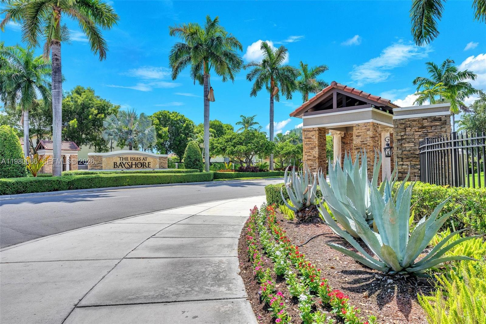 The entrance to The Isles at Bayshore features a stone gatehouse, palm trees, and landscaping — 9011 SW 227th St # 1, Cutler Bay FL 33190, CUTLER BAY, FL