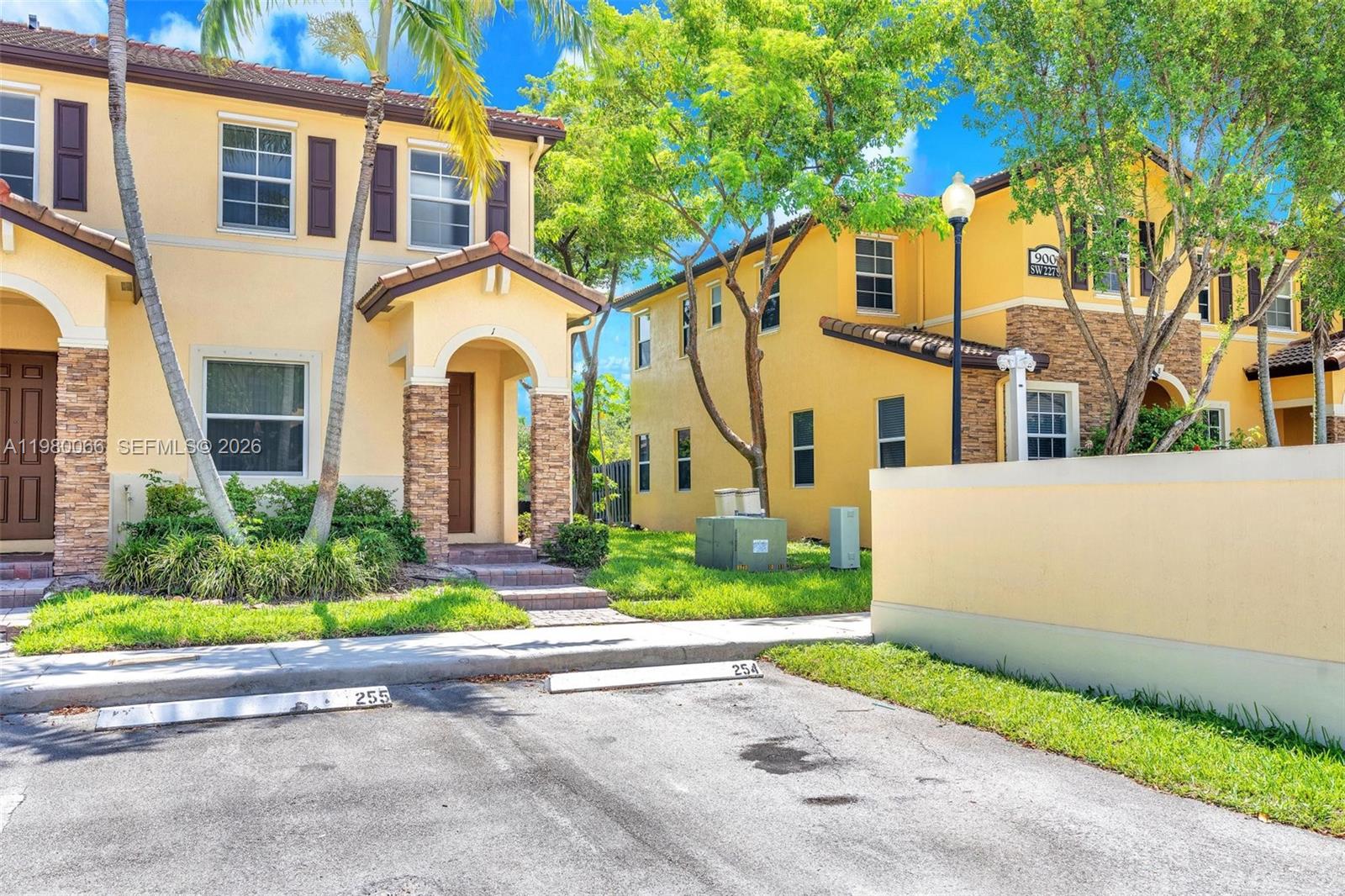 Exterior view of two yellow two-story townhouses with stone accents and assigned parking spaces — 9011 SW 227th St # 1, Cutler Bay FL 33190, CUTLER BAY, FL