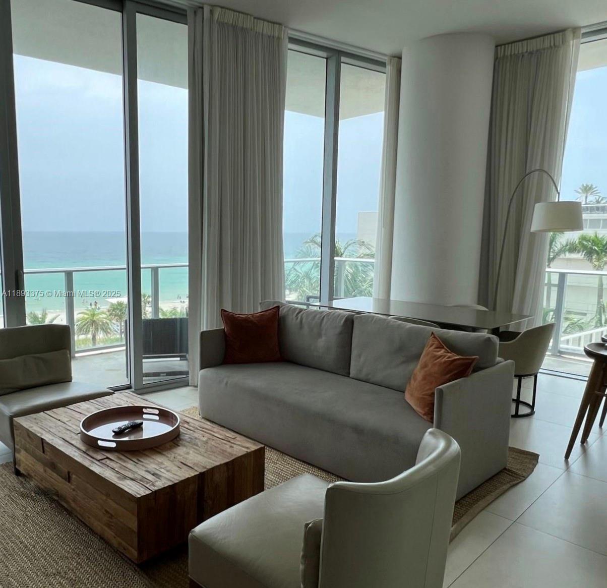 A living room features a gray sofa, wooden coffee table, and floor-to-ceiling windows overlooking the ocean — 4111 S Ocean Dr # 405, Hollywood FL 33019, HOLLYWOOD, FL