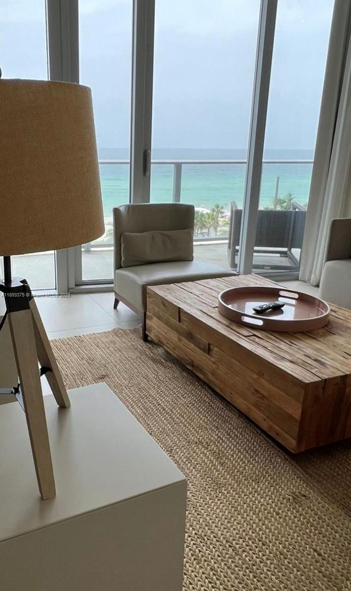 A living room features a wooden coffee table, a beige armchair, and floor-to-ceiling ocean views — 4111 S Ocean Dr # 405, Hollywood FL 33019, HOLLYWOOD, FL