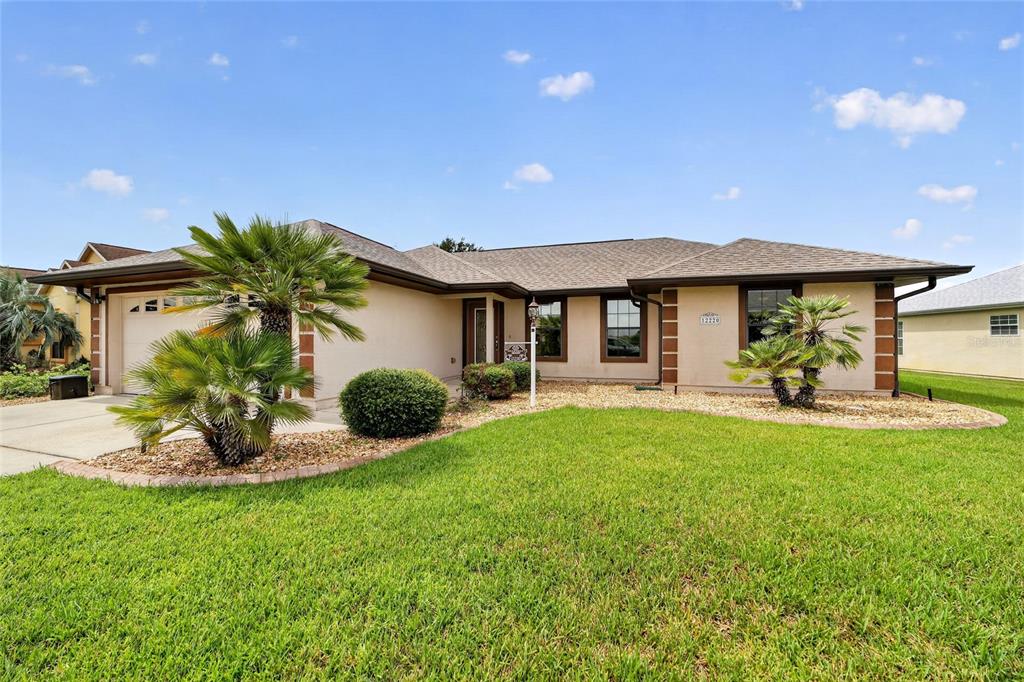 A single-story house with a tan stucco exterior, a brown roof, and palm trees — 12220 SE 172ND LANE, SUMMERFIELD, FL