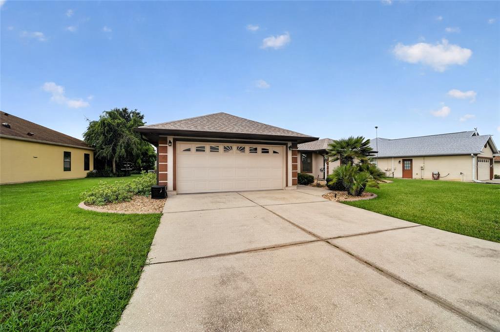 A single-story house with a two-car garage, concrete driveway, and green lawn under a sky — 12220 SE 172ND LANE, SUMMERFIELD, FL