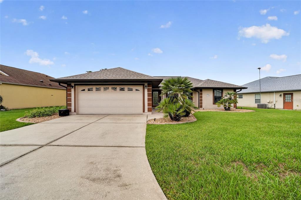 A single-story house with a beige exterior, a two-car garage, and a manicured front lawn — 12220 SE 172ND LANE, SUMMERFIELD, FL