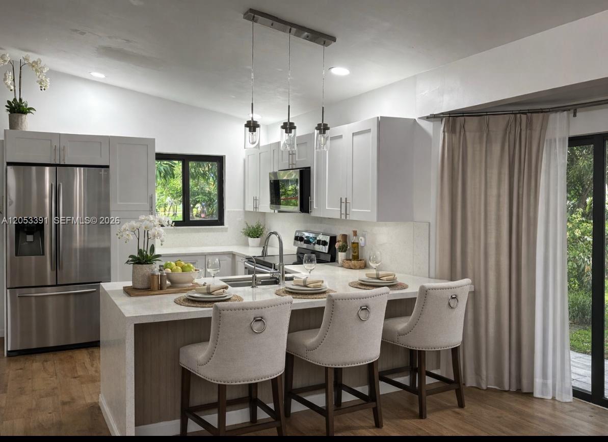 A modern kitchen features white cabinets, stainless steel appliances, and a quartz-topped island with seating — 9821 W Elm Ln # 9821, Miramar FL 33025, MIRAMAR, FL