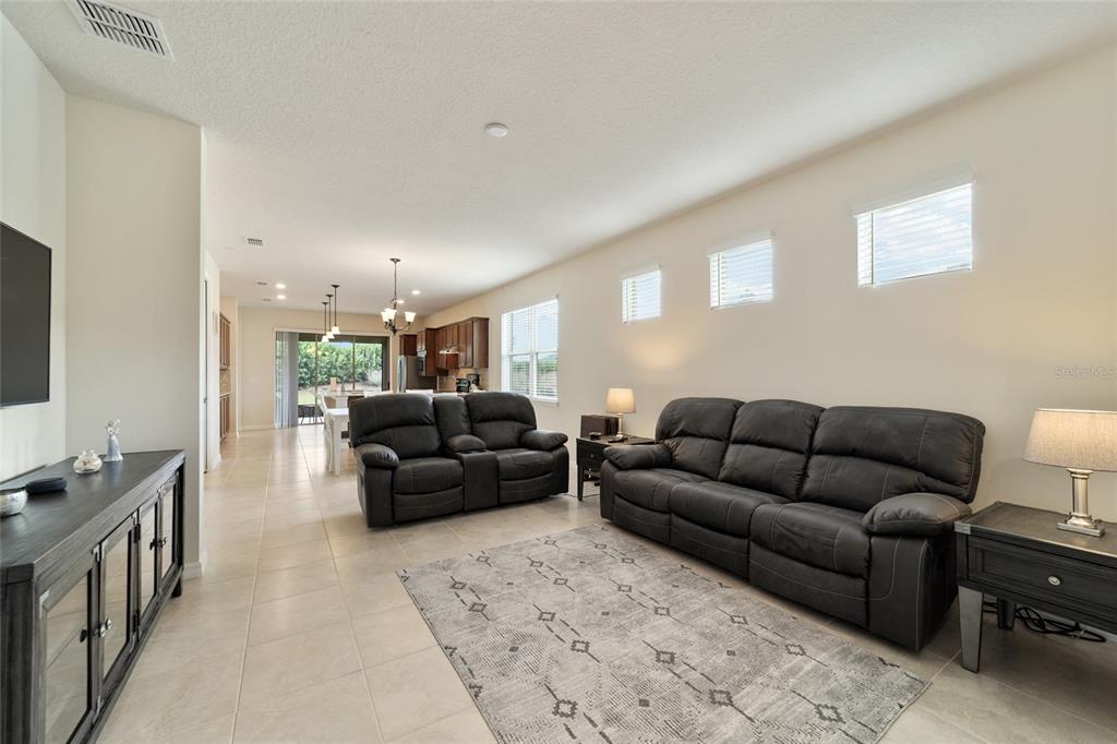 A living room with dark leather sofas, a patterned rug, and an open kitchen beyond — 6094 SW 93RD CIRCLE, OCALA, FL