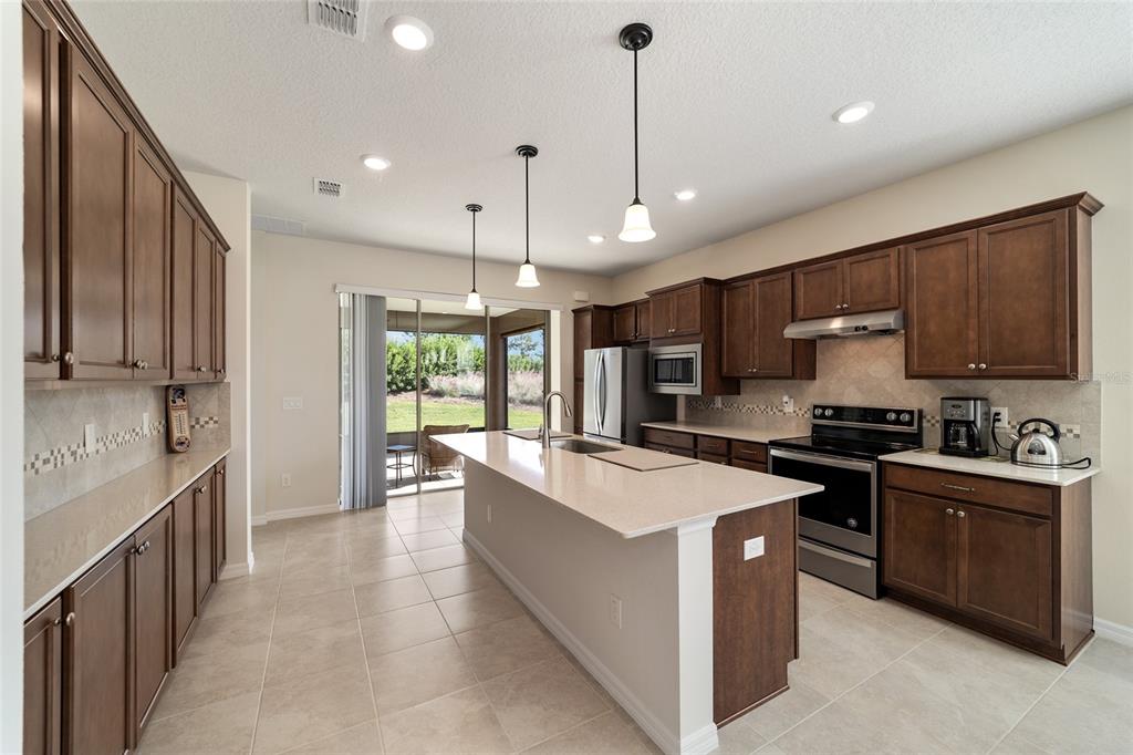 A kitchen features dark wood cabinets, a central island with a sink, and tile flooring — 6094 SW 93RD CIRCLE, OCALA, FL