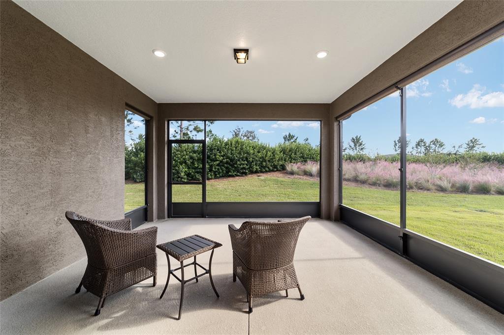 A covered patio features two wicker chairs, a small table, and large screened-in wall panels — 6094 SW 93RD CIRCLE, OCALA, FL