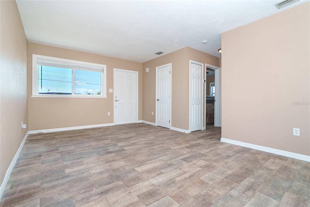 An empty room features light-colored walls, wood-look tile flooring, a window, and several white doors — 138 BUCKEYE AVENUE NW, PORT CHARLOTTE, FL