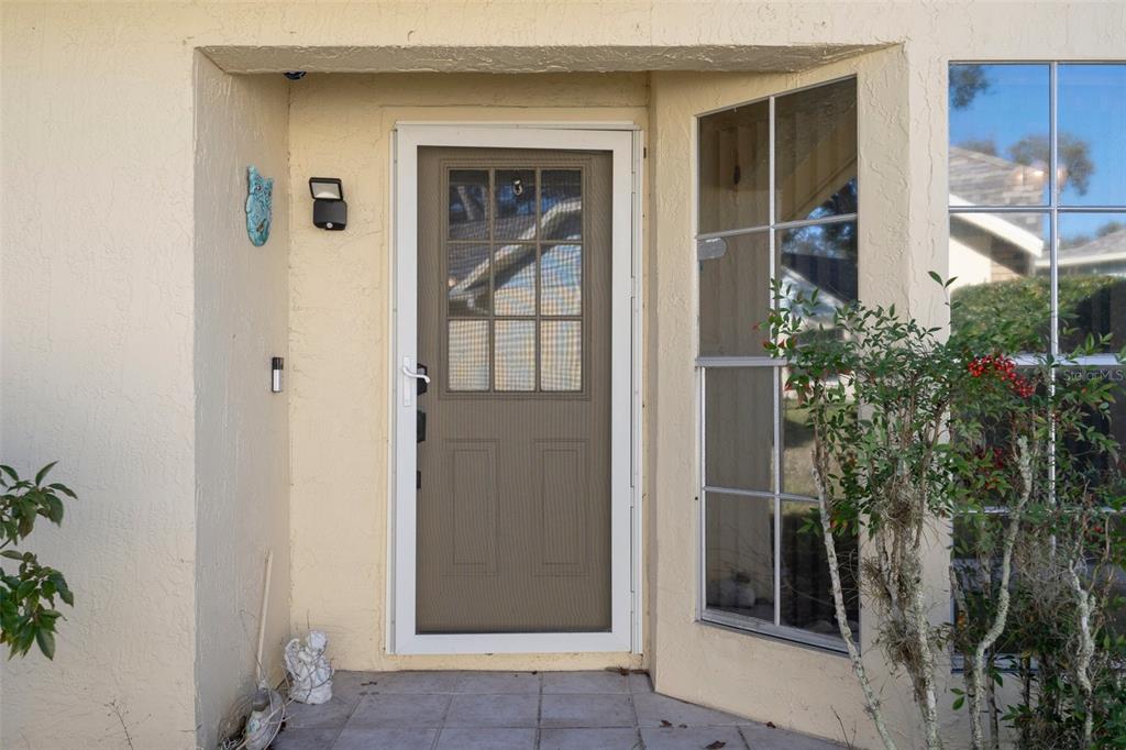 A front entryway features a tan stucco wall, a storm door, and a bay window — 4808 VESPER COURT UNIT 34, NEW PORT RICHEY, FL
