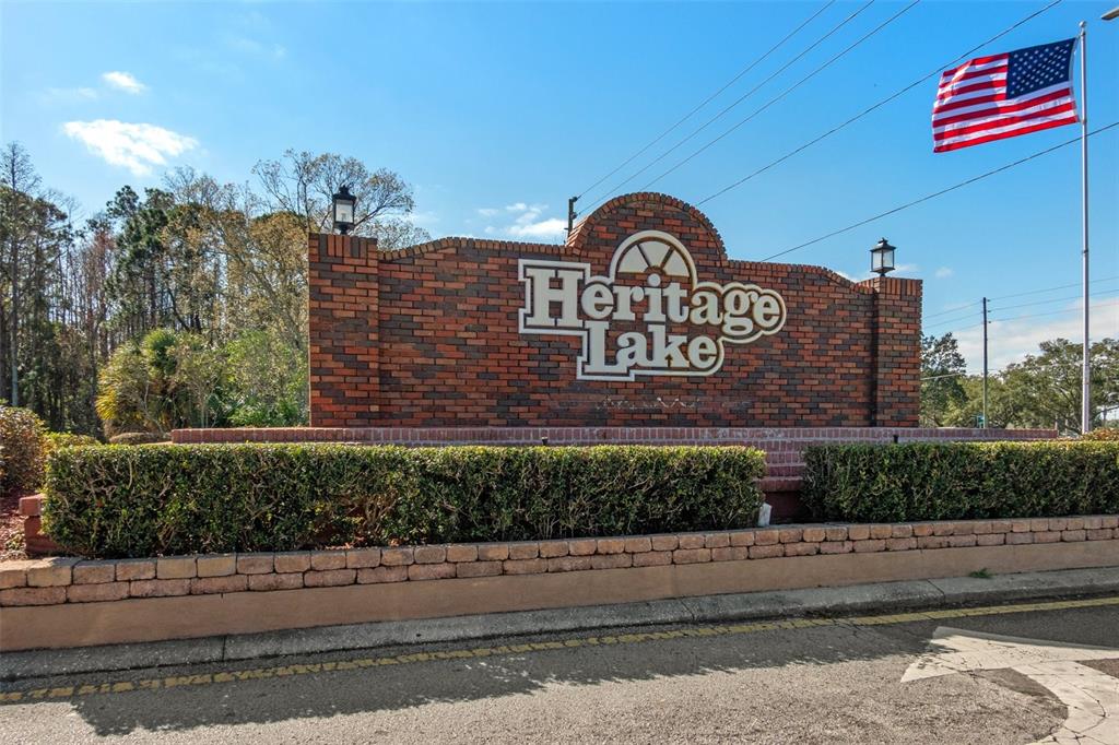 A brick monument sign for Heritage Lake stands behind a hedge with an American flag — 4808 VESPER COURT UNIT 34, NEW PORT RICHEY, FL