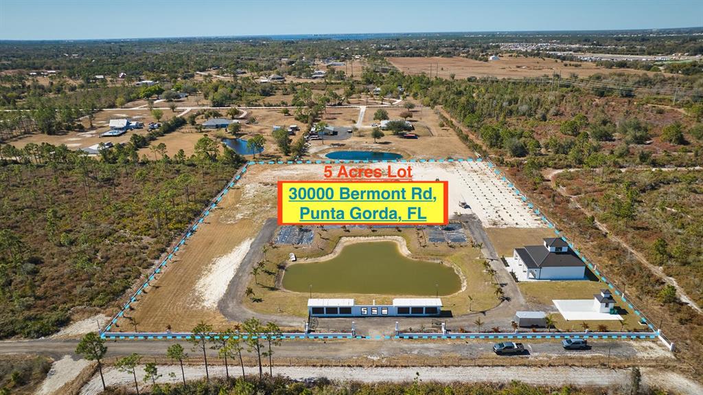 An aerial view shows a fenced five-acre property featuring a large pond and a building — 30000 BERMONT ROAD, PUNTA GORDA, FL