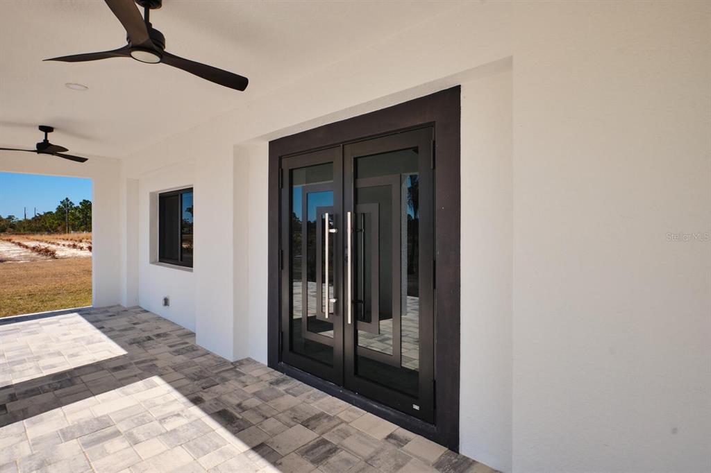 A covered patio features a tiled floor, two ceiling fans, and modern double glass doors — 30000 BERMONT ROAD, PUNTA GORDA, FL