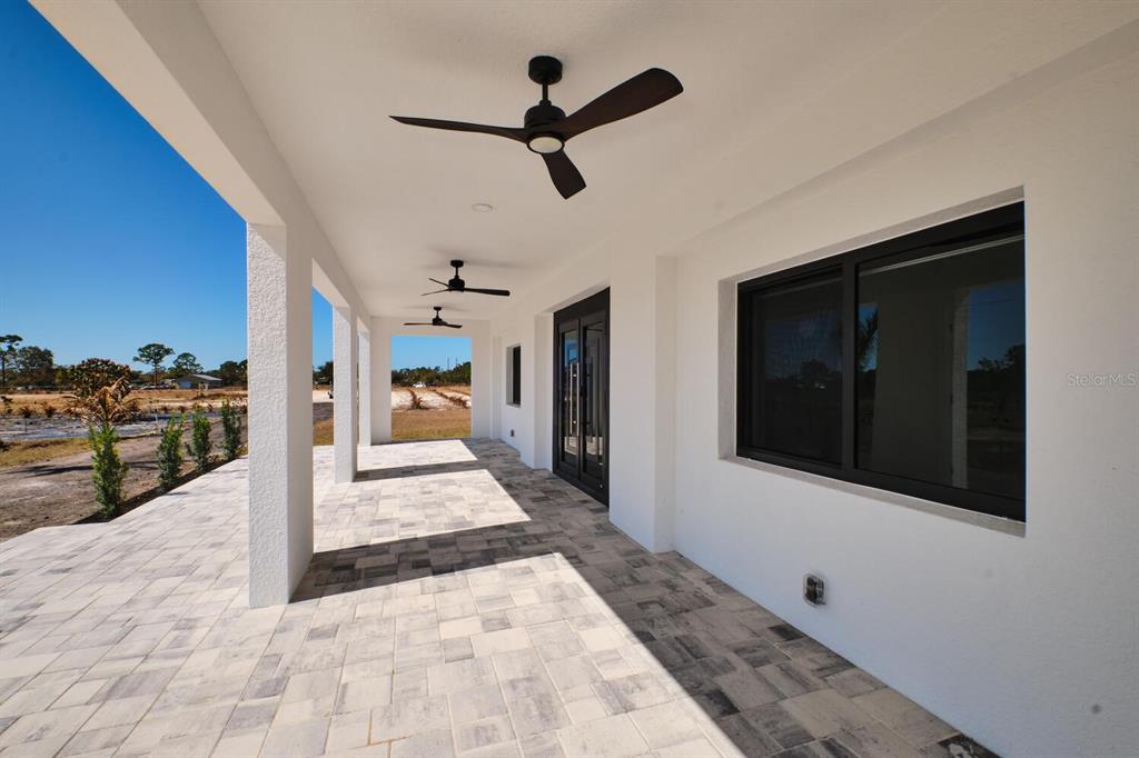 A covered patio with a paved floor, ceiling fans, and white walls overlooks a field — 30000 BERMONT ROAD, PUNTA GORDA, FL