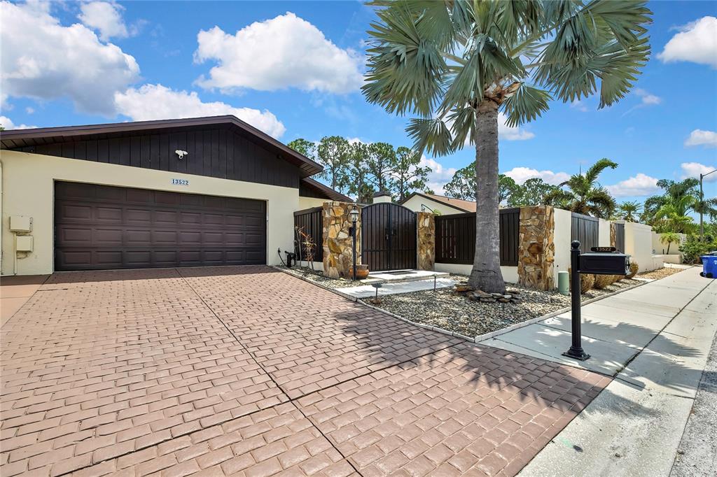 A house exterior features a brown garage, stone pillars, a gated courtyard, and a palm tree — 13522 AVISTA DRIVE, TAMPA, FL