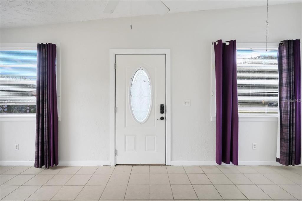 A white front door is centered between two windows with purple curtains and tiled floors — 107 GARRISON DRIVE, SANFORD, FL