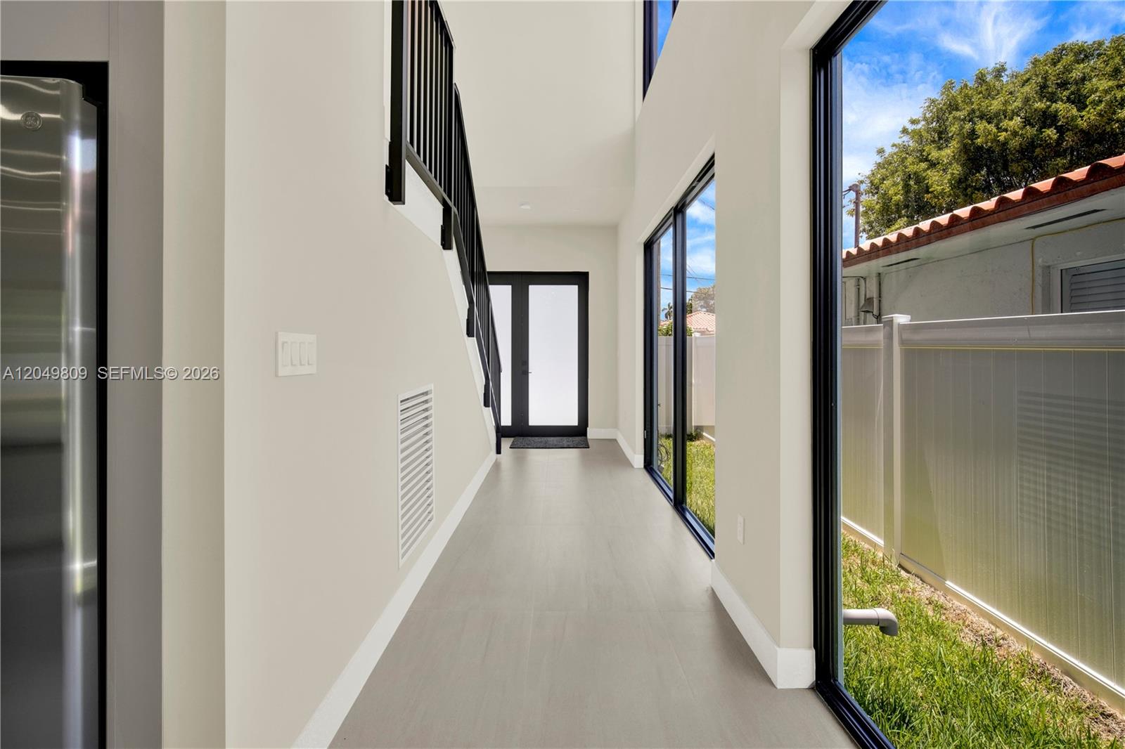 A hallway with light flooring, a black staircase railing, and large windows overlooking a yard — 2889 SW 35 Ave # 2887, Miami FL 33133, MIAMI, FL