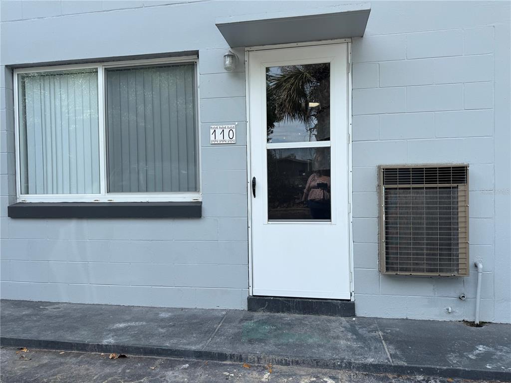 The exterior of a building features a white door labeled 110, a window, and an air conditioner — 825 N PRIMROSE DRIVE UNIT 110, ORLANDO, FL