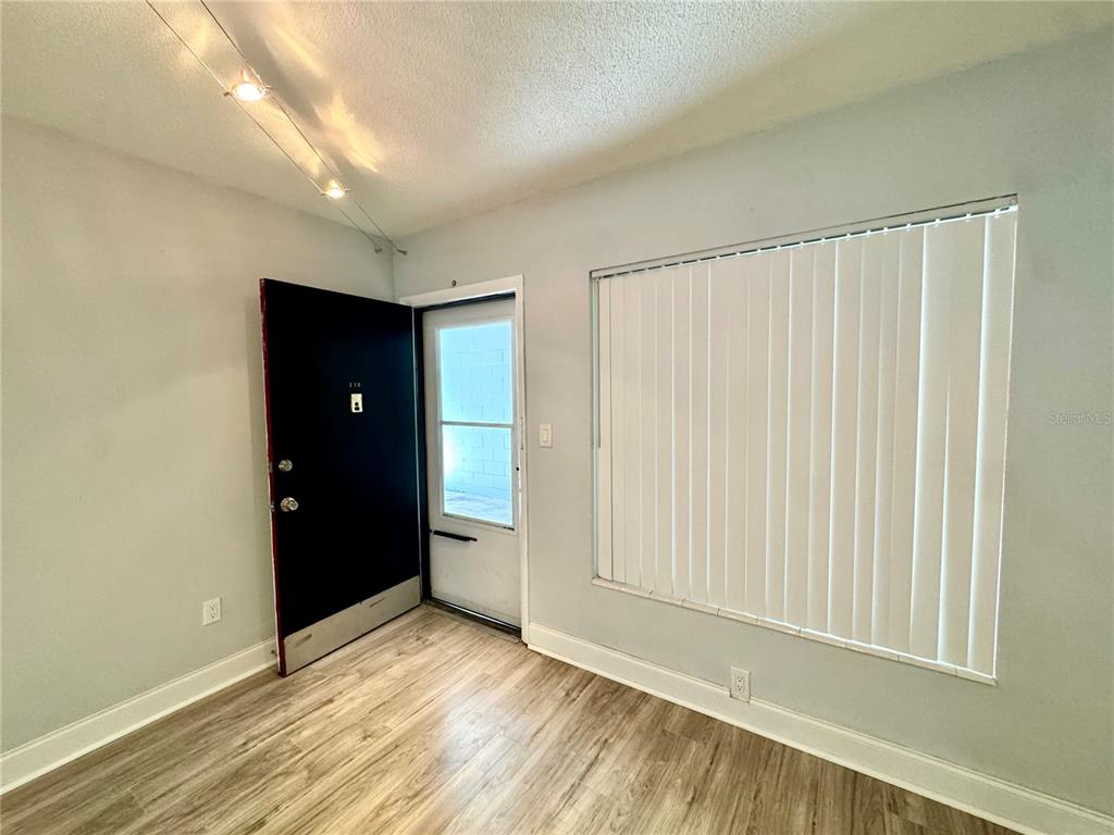 A room with light-colored walls, wood-look flooring, a black door, and vertical window blinds — 825 N PRIMROSE DRIVE UNIT 110, ORLANDO, FL