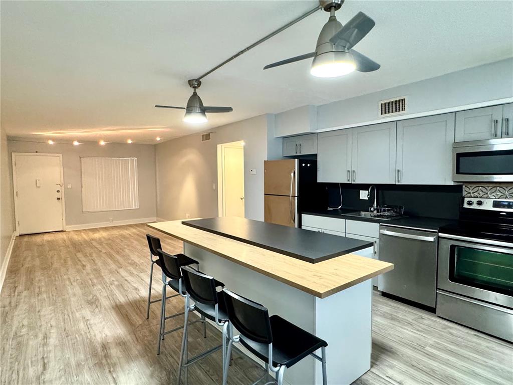 An open-concept kitchen and living area features light wood flooring, gray cabinetry, and a breakfast bar — 825 N PRIMROSE DRIVE UNIT 110, ORLANDO, FL