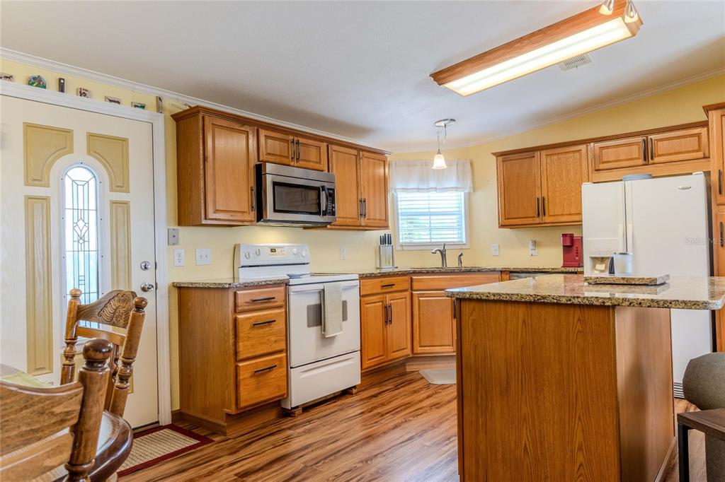 A kitchen features wood cabinets, granite countertops, a white stove, and wood-look flooring — 2100 KINGS HIGHWAY UNIT 977, PORT CHARLOTTE, FL