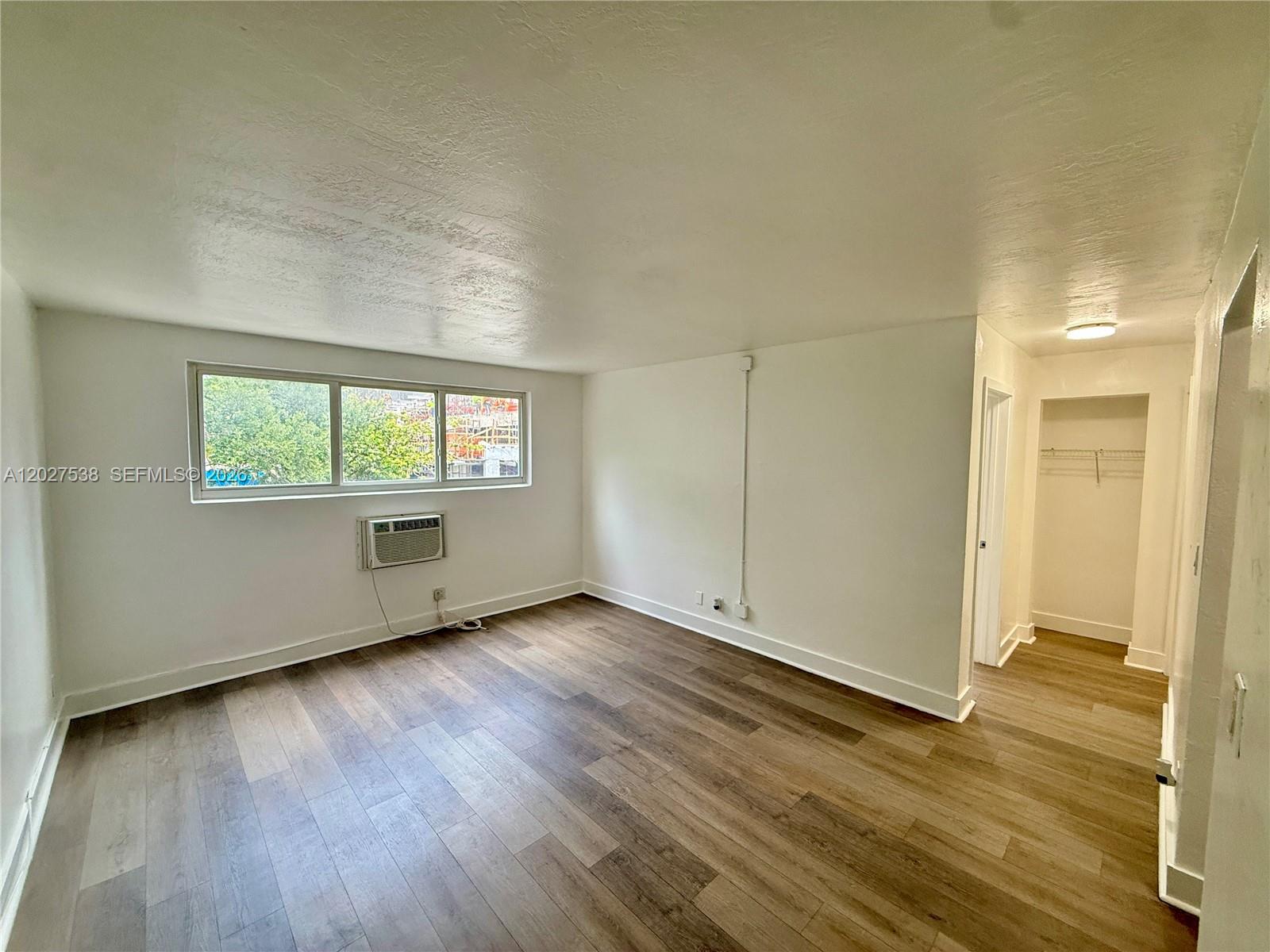 An empty room features wood-look flooring, white walls, a window air conditioner, and a closet — 143 SW 9th St # 206, Miami FL 33130, MIAMI, FL