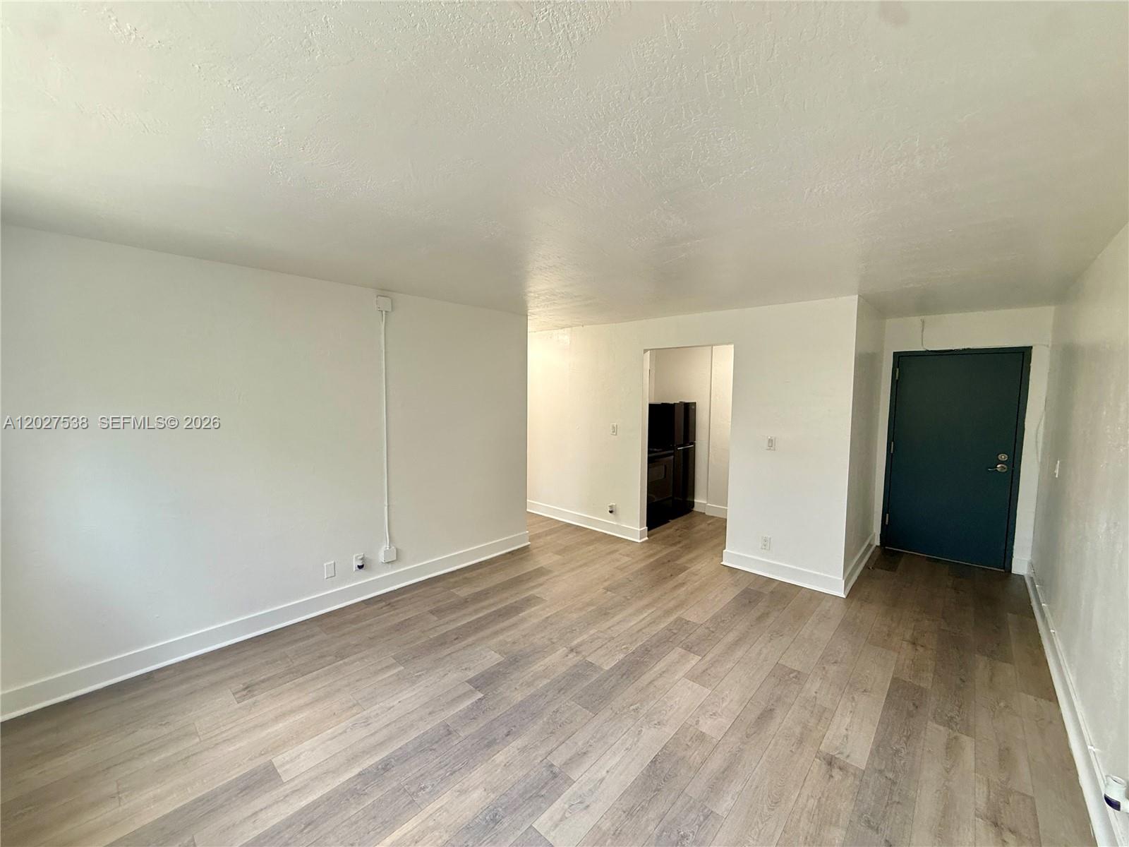 An empty room with light wood-look flooring, white walls, and a dark blue door — 143 SW 9th St # 206, Miami FL 33130, MIAMI, FL