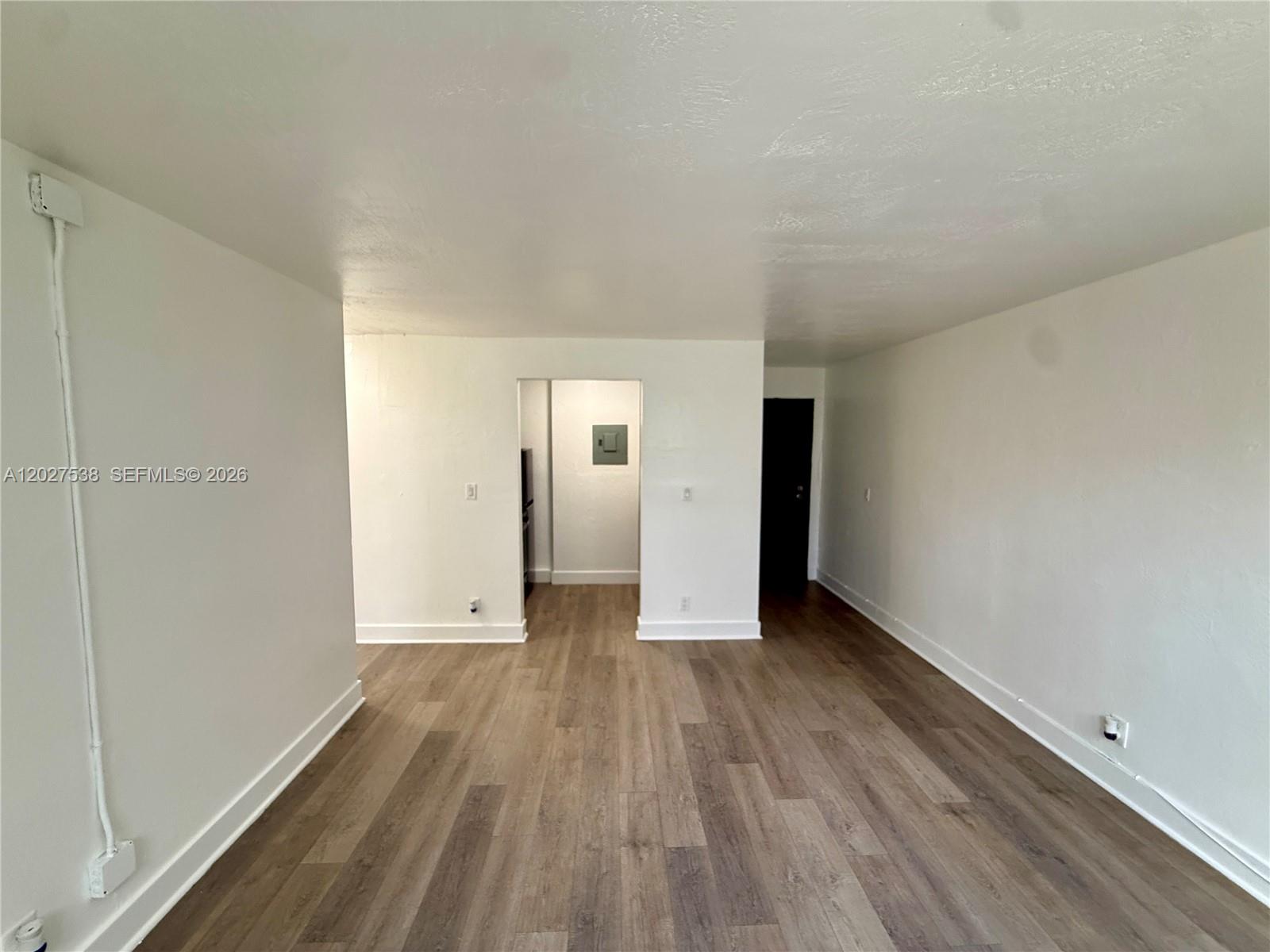 An empty room features white walls, wood-look flooring, and a doorway leading to a kitchen — 143 SW 9th St # 206, Miami FL 33130, MIAMI, FL