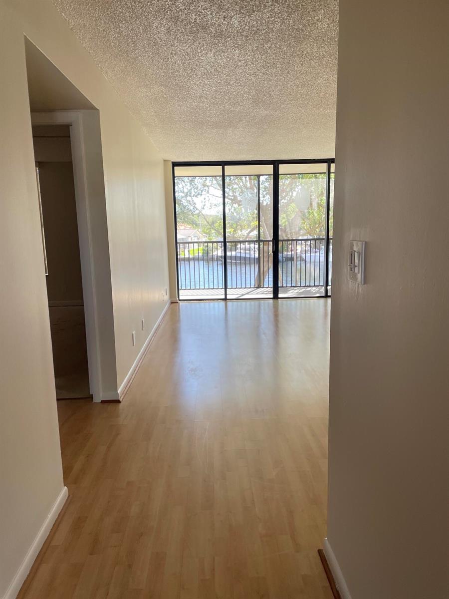 An interior view of a living area with wood-look flooring leading to a waterfront balcony — 14 Royal Palm Way # 204, Boca Raton FL 33432, BOCA RATON, FL