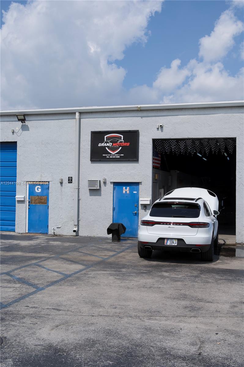 A white Porsche SUV is parked outside a commercial building with blue doors and signage — 7215 NW 41st St # H, Miami FL 33166, MIAMI, FL