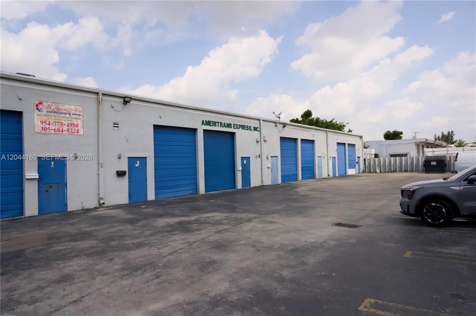 A row of industrial warehouse units features blue roll-up doors and pedestrian entrances — 7215 NW 41st St # H, Miami FL 33166, MIAMI, FL