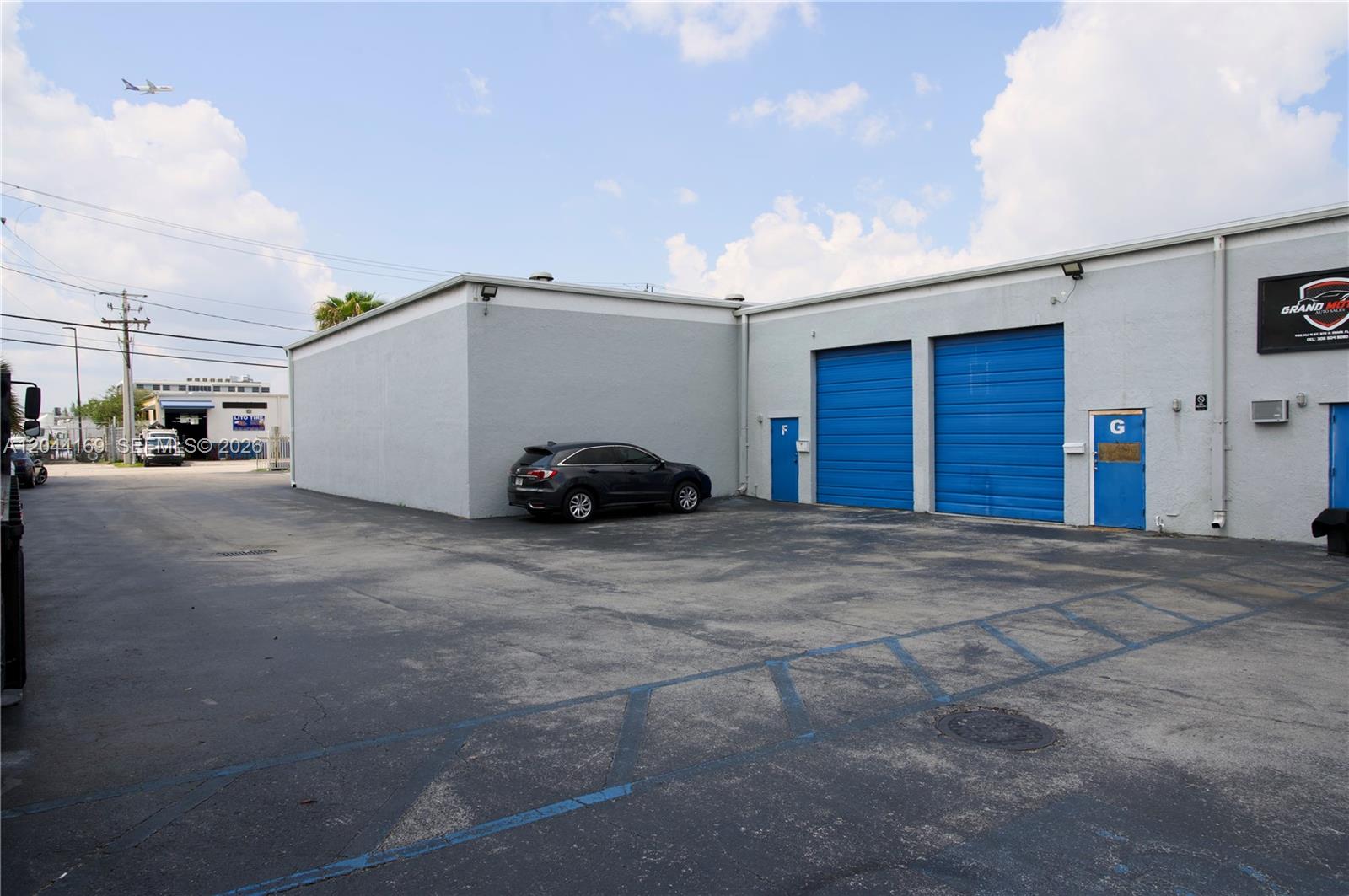 A gray commercial building with blue roll-up doors and a parked car in the lot — 7215 NW 41st St # H, Miami FL 33166, MIAMI, FL