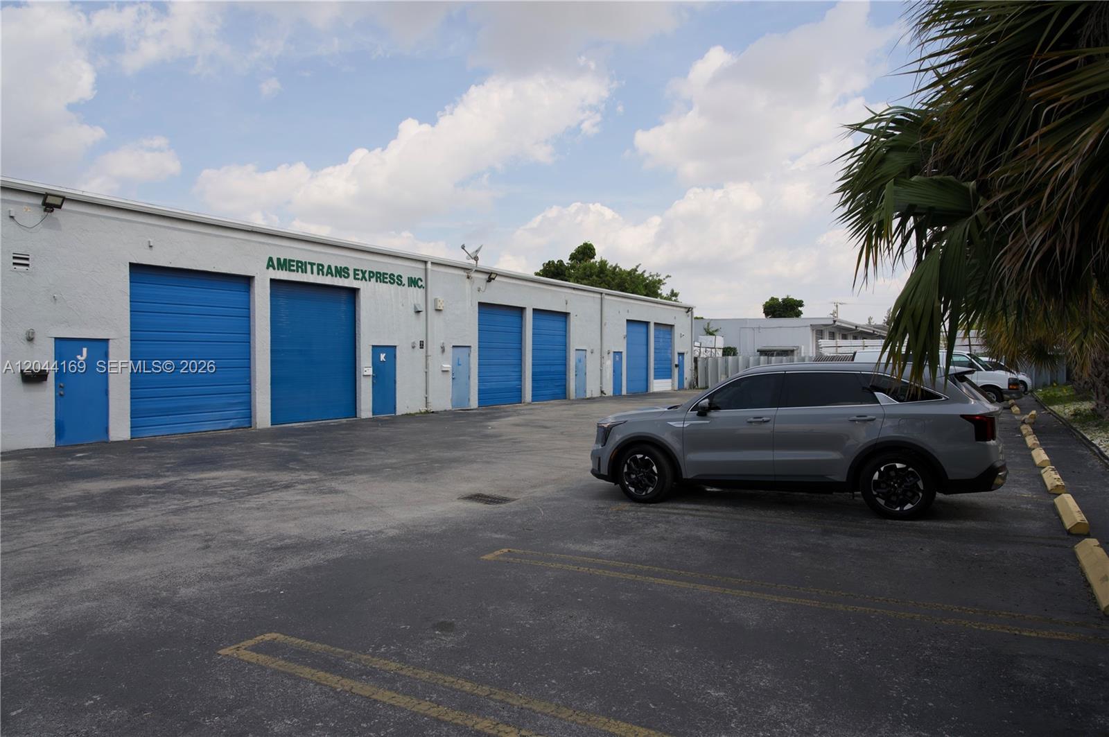 A gray SUV is parked in front of a commercial warehouse building with blue doors — 7215 NW 41st St # H, Miami FL 33166, MIAMI, FL