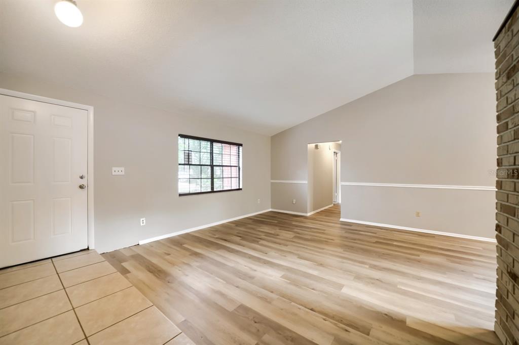 An empty living room features light wood-look flooring, a vaulted ceiling, and a brick fireplace — 717 LANCEWOOD DRIVE, WINTER SPRINGS, FL