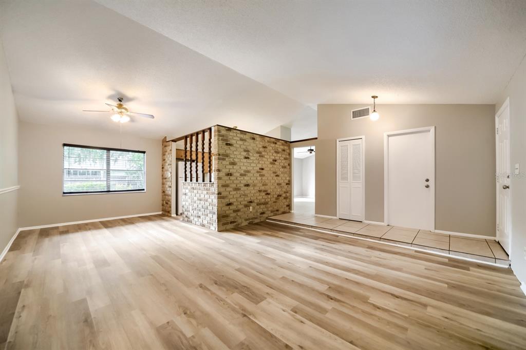 A living room with light wood-look flooring, a brick accent wall, and a tiled entryway — 717 LANCEWOOD DRIVE, WINTER SPRINGS, FL