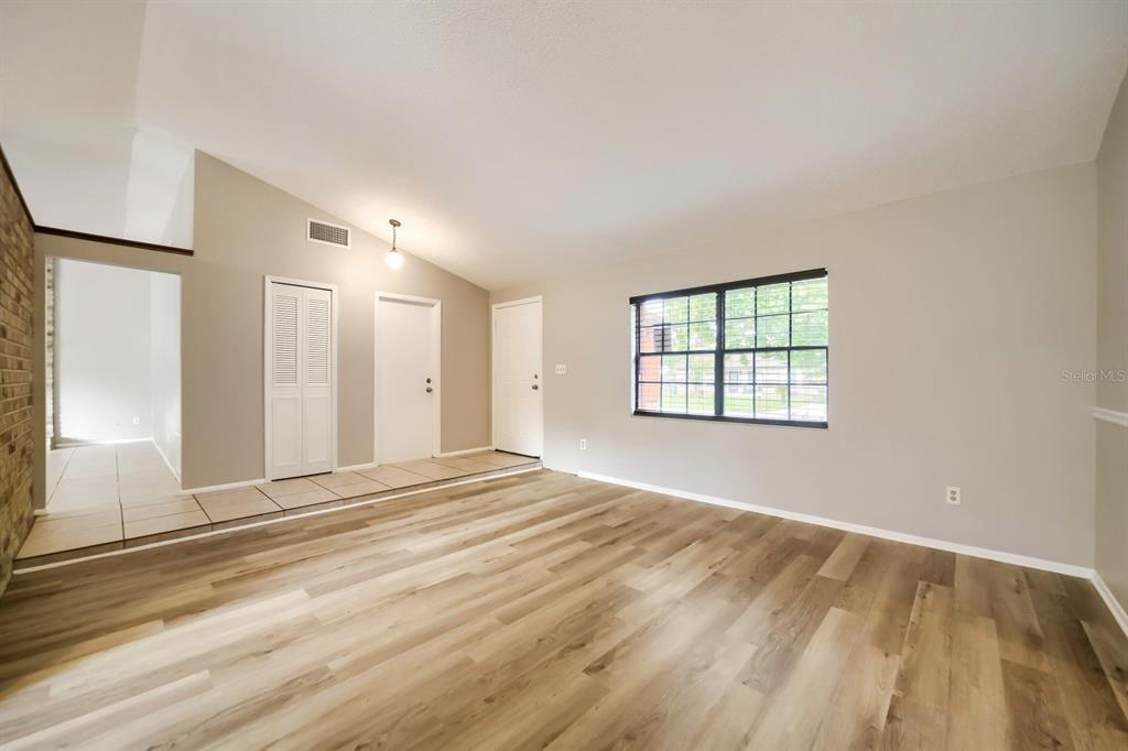 An empty living room features light wood-look flooring, beige walls, and a large window — 717 LANCEWOOD DRIVE, WINTER SPRINGS, FL