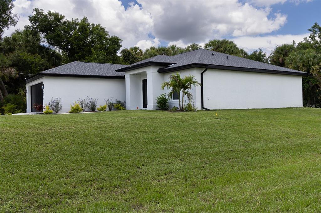A white, single-story house with a dark roof sits on a large, grassy lawn — 4696 APRIL AVENUE, NORTH PORT, FL