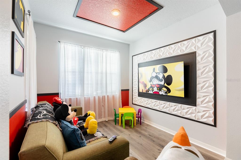 A Mickey Mouse-themed playroom features a wall-mounted television, a sofa, and a small table — 891 ASSEMBLY COURT, REUNION, FL