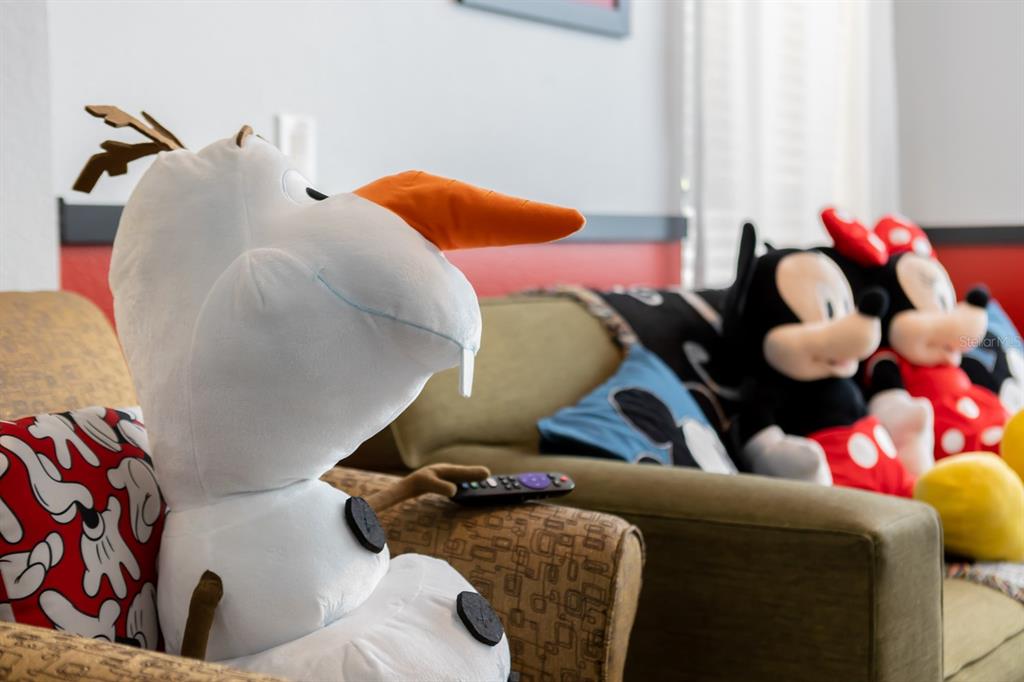 A plush Olaf toy sits in an armchair holding a remote near a sofa with Disney-themed pillows — 891 ASSEMBLY COURT, REUNION, FL