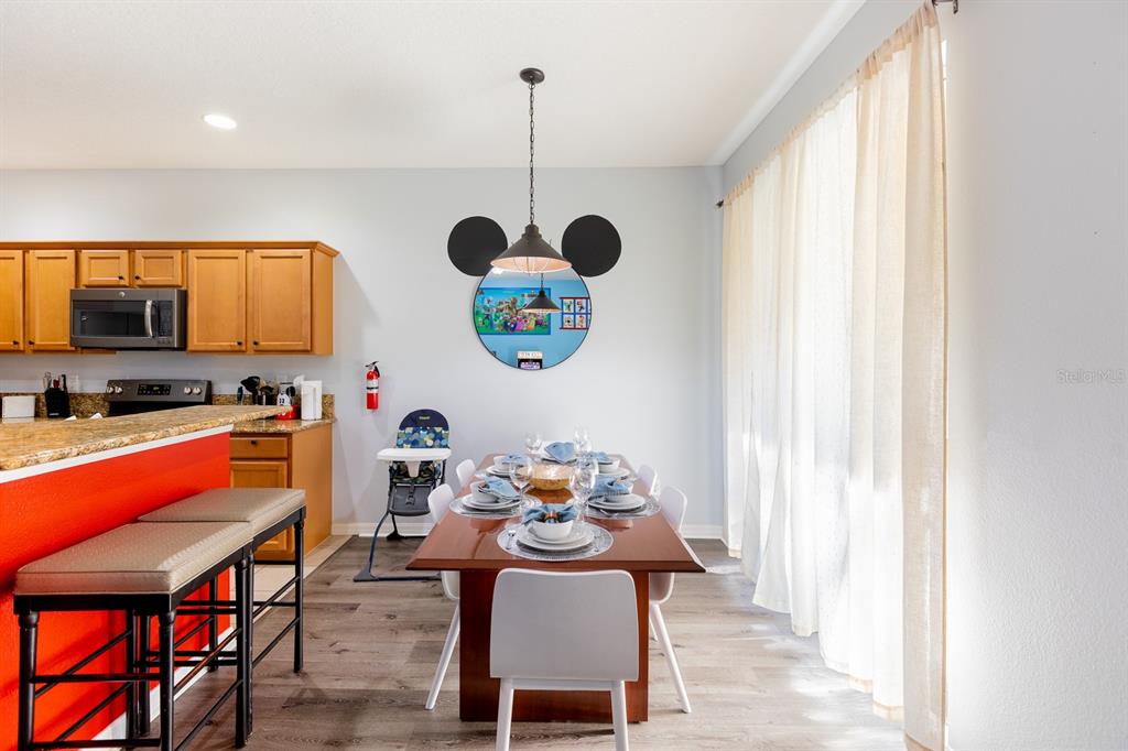 A dining area features a wooden table, Mickey Mouse-themed wall decor, and a kitchen island — 891 ASSEMBLY COURT, REUNION, FL