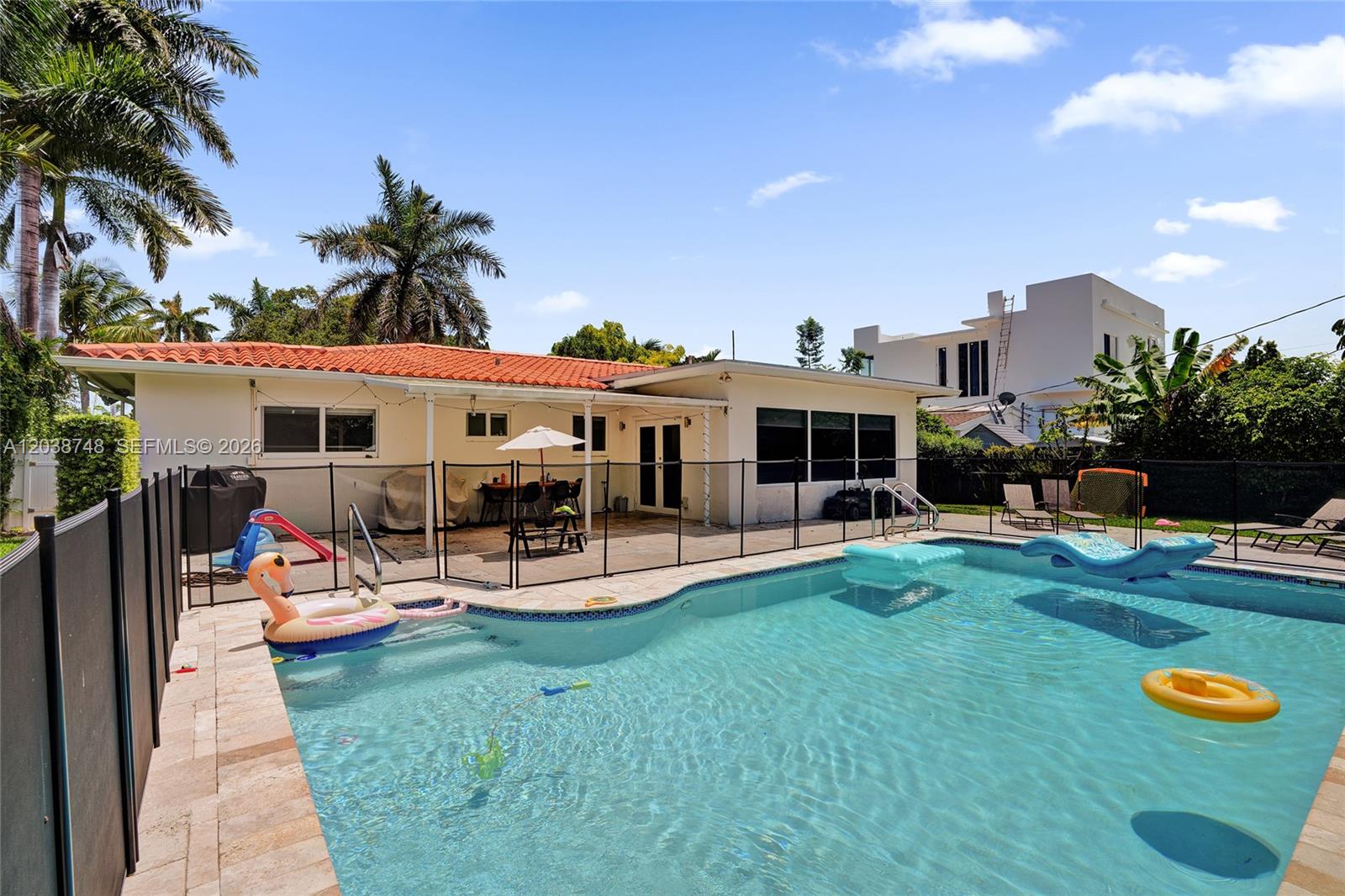 A backyard features a swimming pool with floating toys, a patio, and a single-story house — 2025 Alamanda Dr, North Miami FL 33181, NORTH MIAMI, FL