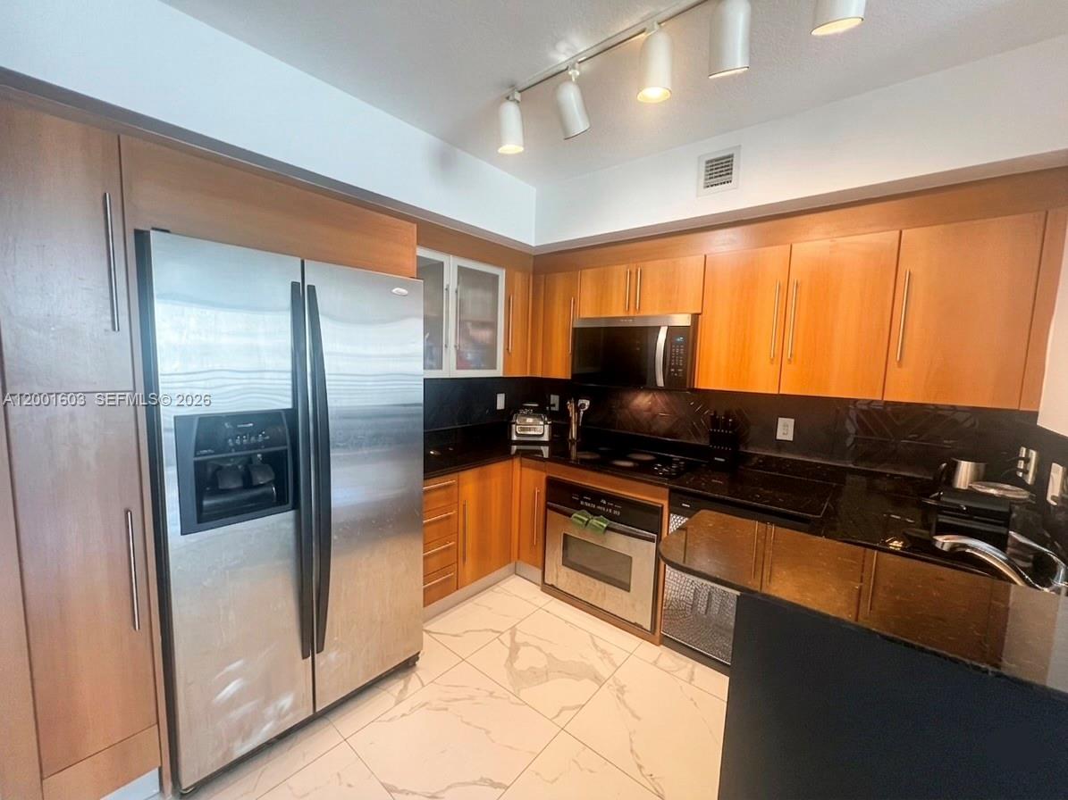 A kitchen features wood cabinets, stainless steel appliances, black countertops, and light-colored tiled flooring — 335 S Biscayne Blvd # 3300, Miami FL 33131, MIAMI, FL
